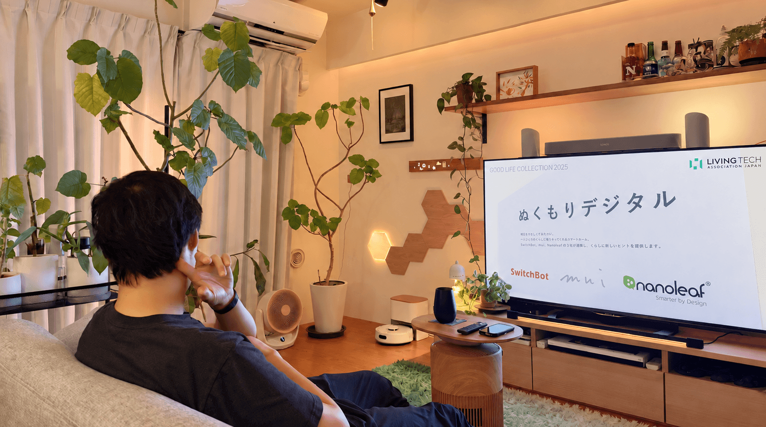 木目の家具や観葉植物、壁の照明を取り入れたリビングでくつろぐ様子
